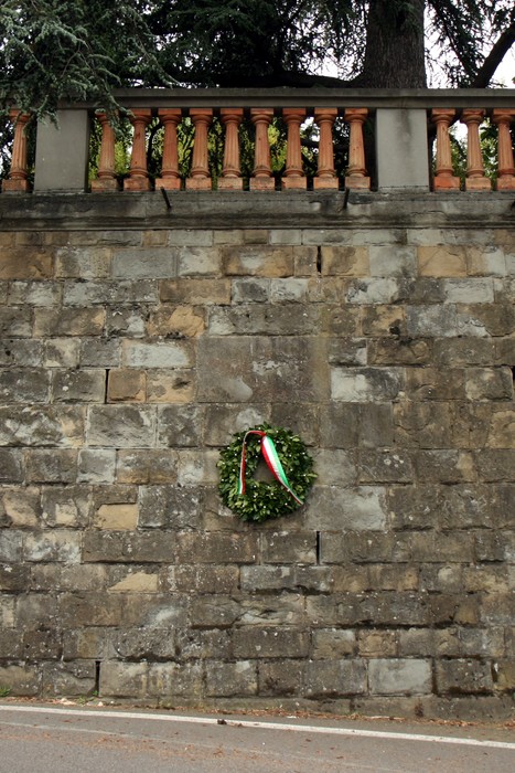 Lapide storica a Giugni, con corona d'alloro e nastro tricolore su un muro in pietra.