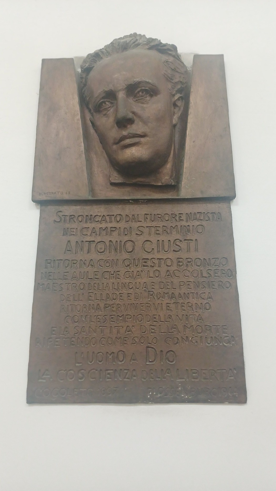 Lapide in bronzo con volto in rilievo di Antonio Giusti e iscrizione, affissa su parete chiara.