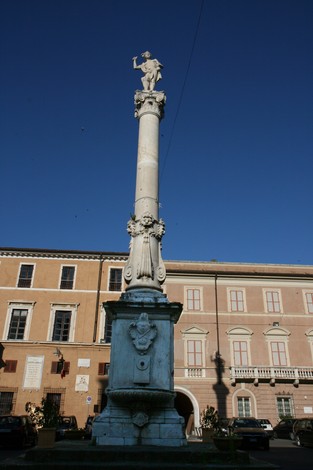 Statua del Mercurio su colonna, piazza con edifici storici sullo sfondo in una giornata soleggiata.