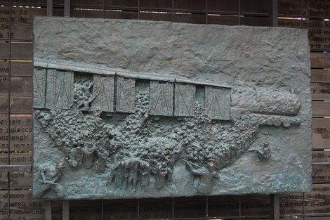 Rappresentazione scultorea di un treno in movimento, circondato da uomini e donne che vivono un momento storicamente significativo.