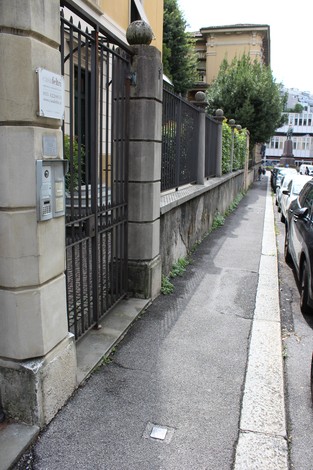 Pietra d'inciampo a Bruni su un marciapiede accanto a una cancellata, in un contesto urbano.