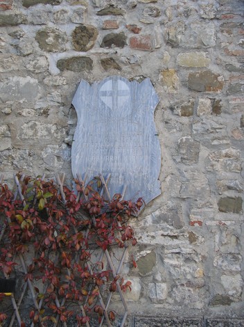 Lapide commemorativa su una parete di pietra, avvolta in piante rampicanti.