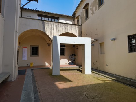 Scorcio di un cortile con architettura semplice e un'opera d'arte moderna al centro. Illuminazione naturale diffusa.