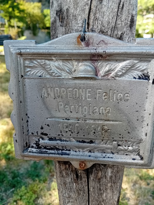 Una targa metallica fissata su un palo di legno nel Parco della Rimembranza, con il nome di una persona e date commemorative.