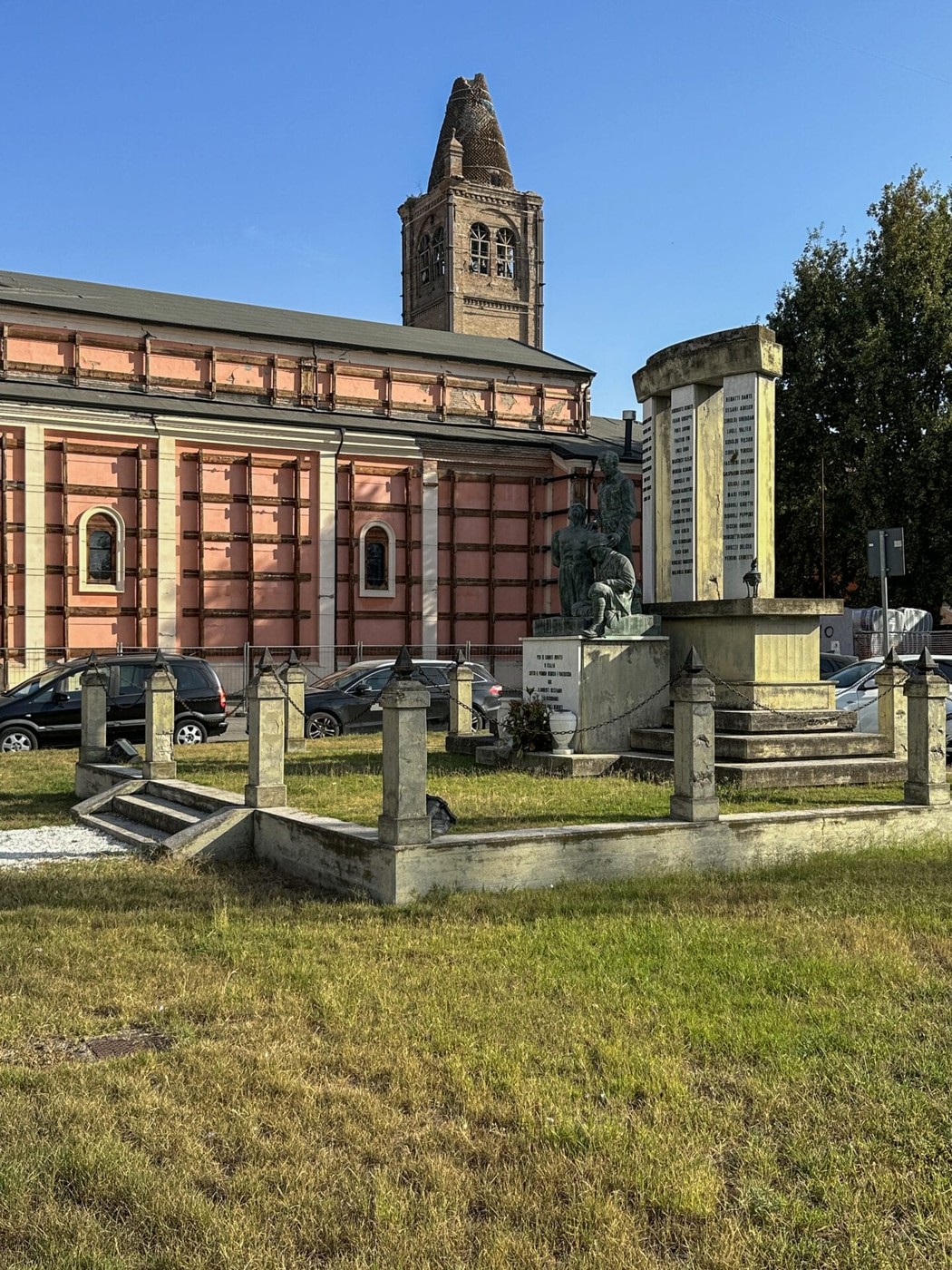 Monumento ai caduti di Rovereto, con un'inscrizione commemorativa e la chiesa sullo sfondo.