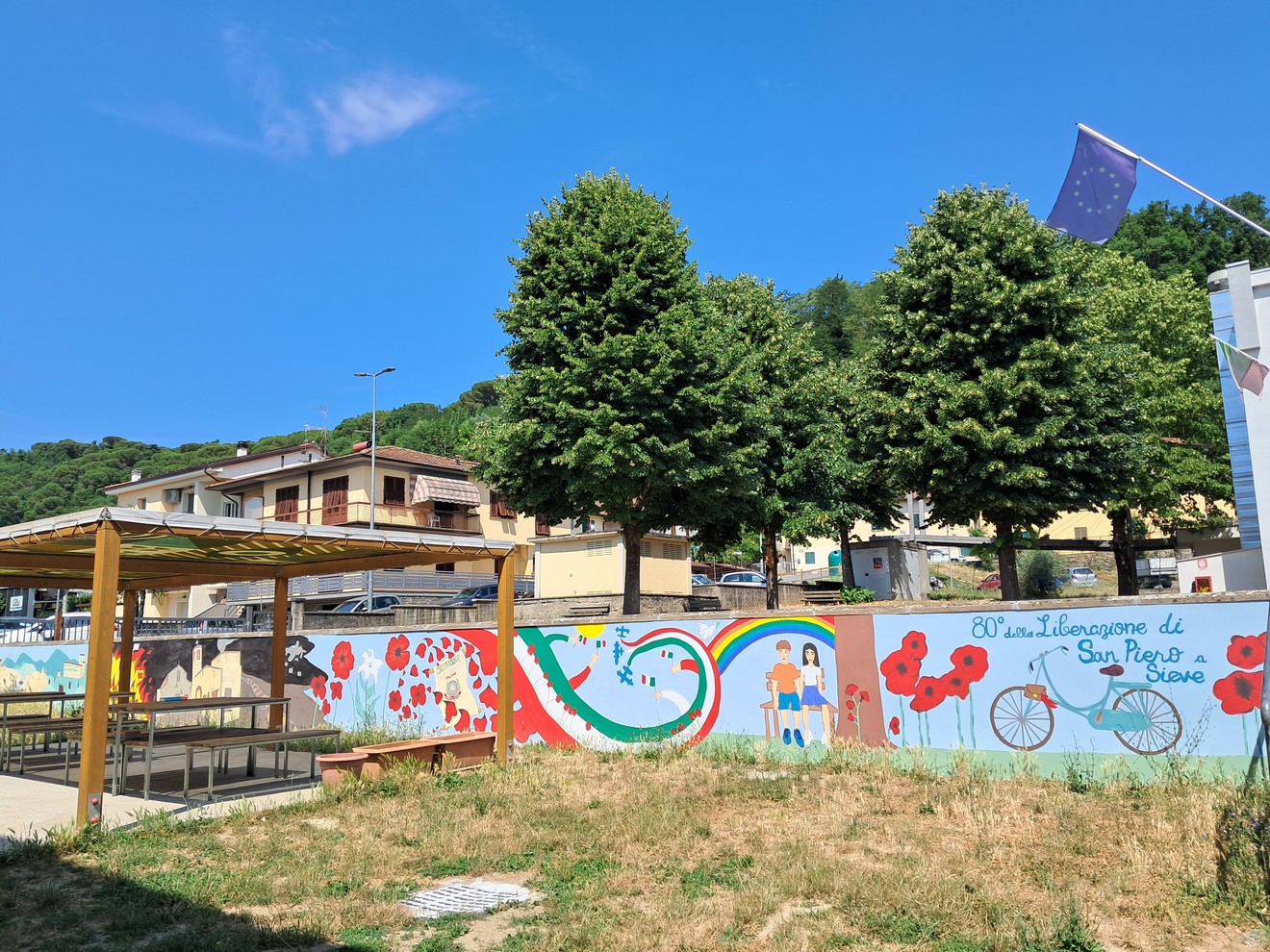 Murale colorato per l'80° della Liberazione di San Piero, con elementi artistici e paesaggio urbano.