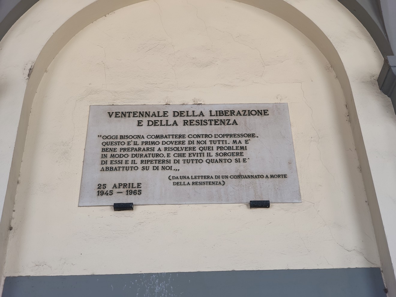 Lapide in marmo con iscrizione, fissata alla parete sotto un arco d'ingresso.