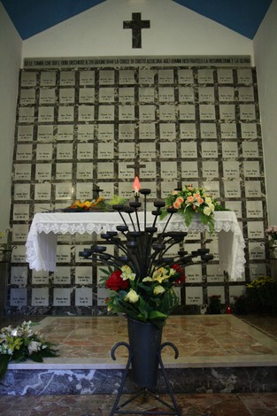 Cappella dei Martiri, un luogo di memoria con altarino fiorito e pareti adornate da omaggi commemorativi.