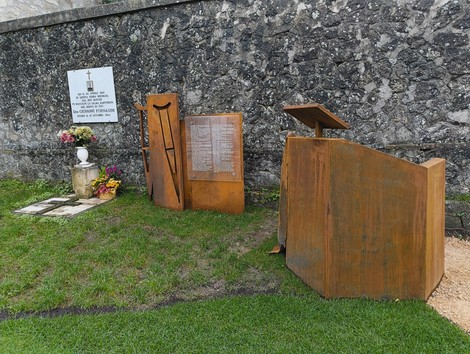 Memoriale dedicato al "Percorso per Fornasini", con opere in metallo e fiori, immerso nella natura.
