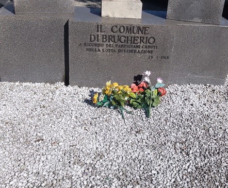 Monumento commemorativo ai partigiani caduti, con fiori colorati e pietre bianche sul terreno circostante.