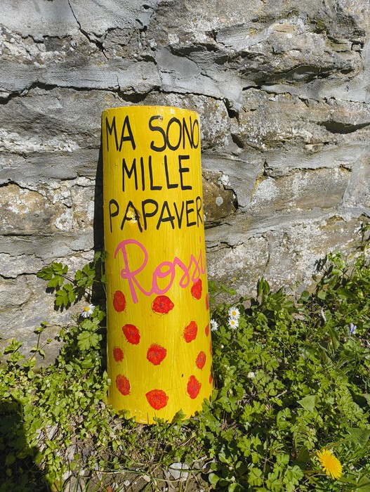Monumento giallo decorato con scritte e fiori colorati, posizionato accanto a un muro di pietra.