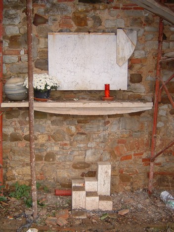 Lapide di Palazzaccio d'Arceno, con base in pietra e omaggio floreale in un contesto rustico.