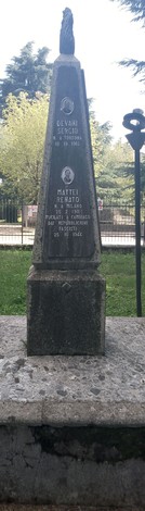 Monumento agli antifascisti, obelisco con dettagli commemorativi e un basamento in pietra, circondato da verde.