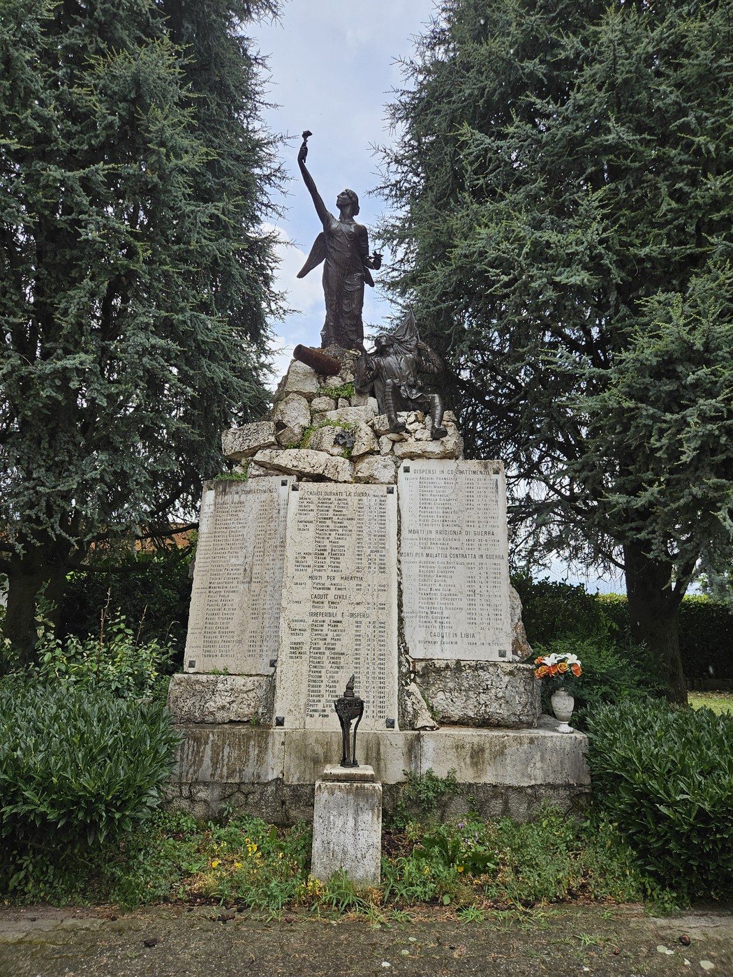 Monumento ai Caduti di Pozzaglio avvolto da verde, con una statua e lapidi commemorative.