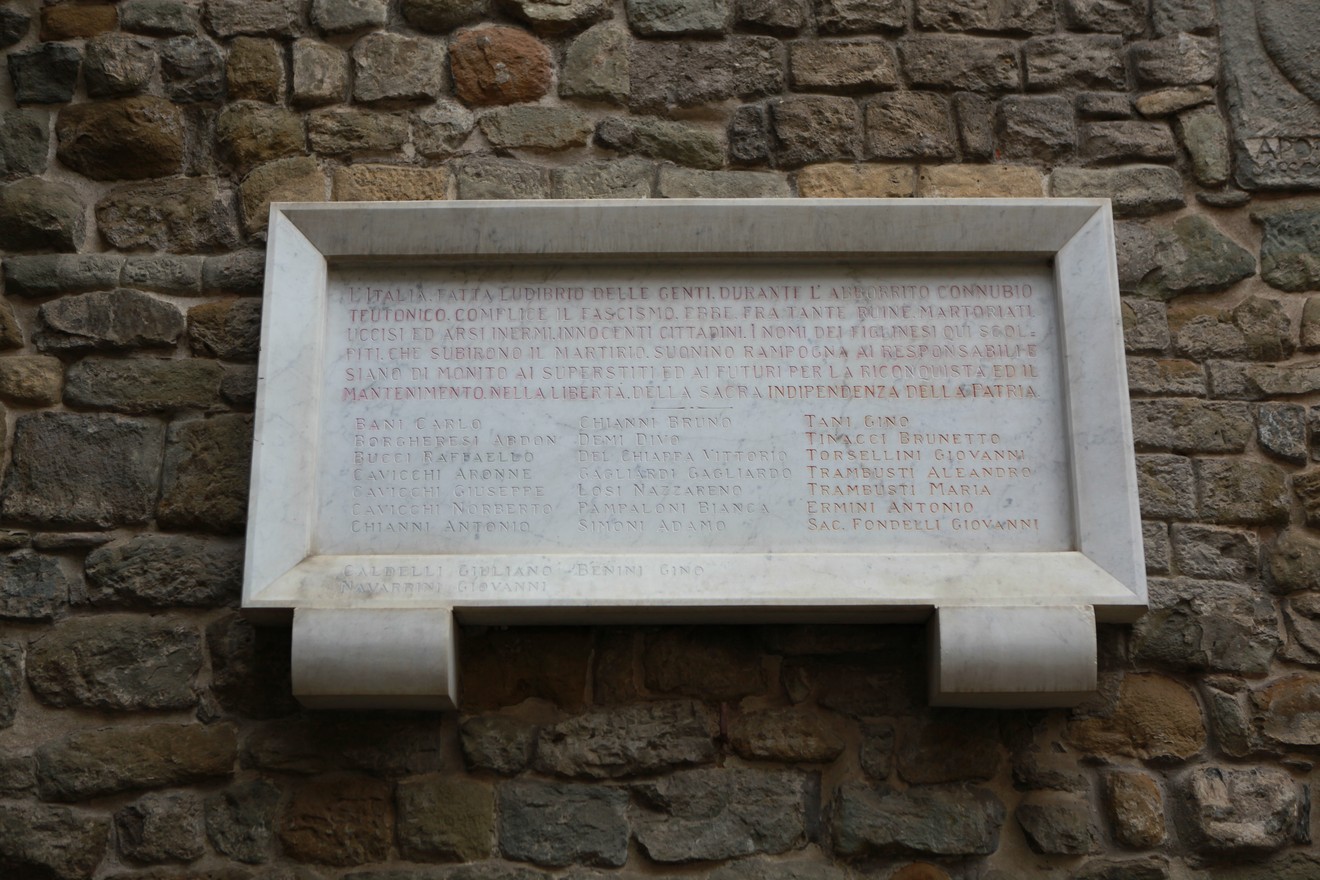 Lapide commemorativa in onore dei caduti per la libertà, incisa su muro di pietra.
