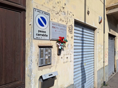 Lapide commemorativa di Minetto sulla facciata di un edificio a Torino, decorata con fiori.
