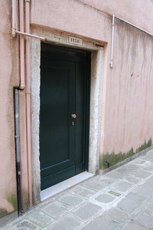 Porta verde in un vicolo, con pareti rosa e pavimento in pietra, che richiama l'atmosfera di un luogo storico.