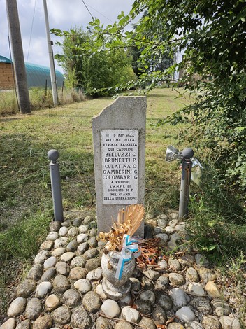 Cippo commemorativo con nomi di vittime della resistenza, decorato con fiori e posti su un basamento di pietre.