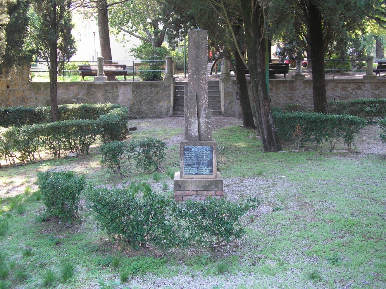Monumento ai caduti immerso nel verde, circondato da alberi e cespugli, in un'atmosfera di commemorazione.