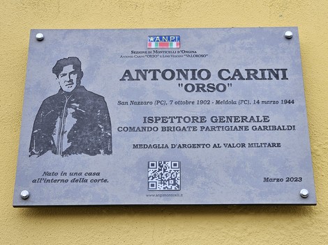 Targa commemorativa in pietra su parete, con ritratto inciso, logo ANPI e codice QR.