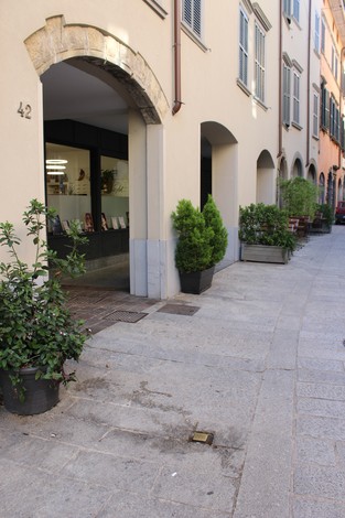 Pietra d'inciampo in un vicolo con piante e un edificio caratteristico sullo sfondo, a Ghezzi.