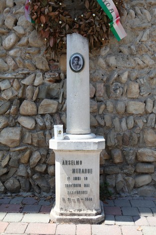 Cippo commemorativo di Anselmo Menabue, con foto e decorazioni, su sfondo di pietre.