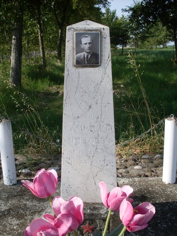 Cippo commemorativo dedicato a Campanini, con foto e fiori, immerso nella natura.