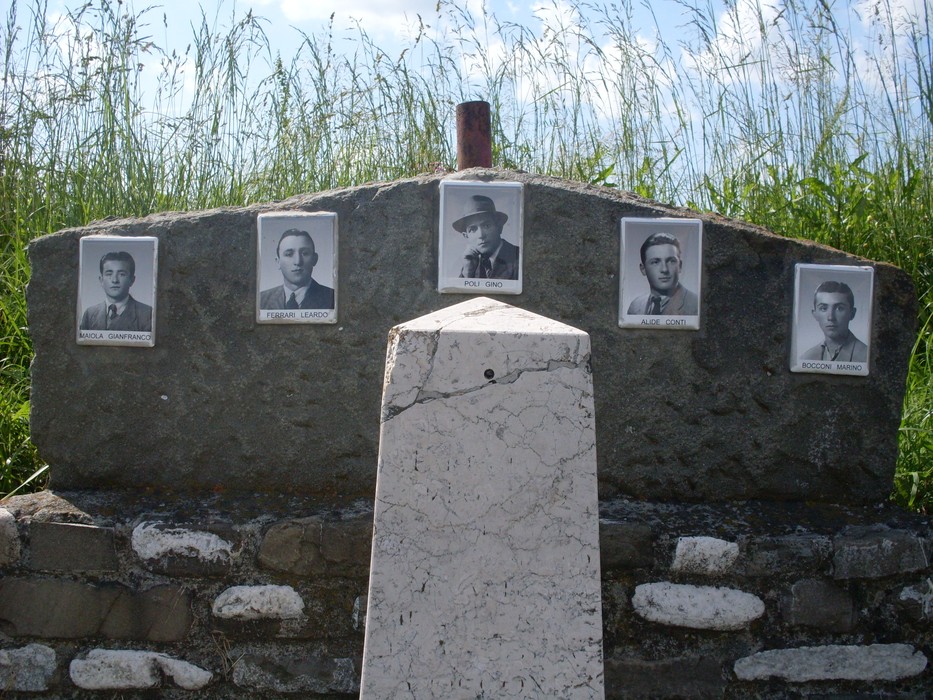 Cippo commemorativo con fotografie di soldati caduti, immerso nella natura. Omaggio alla memoria e al sacrificio.