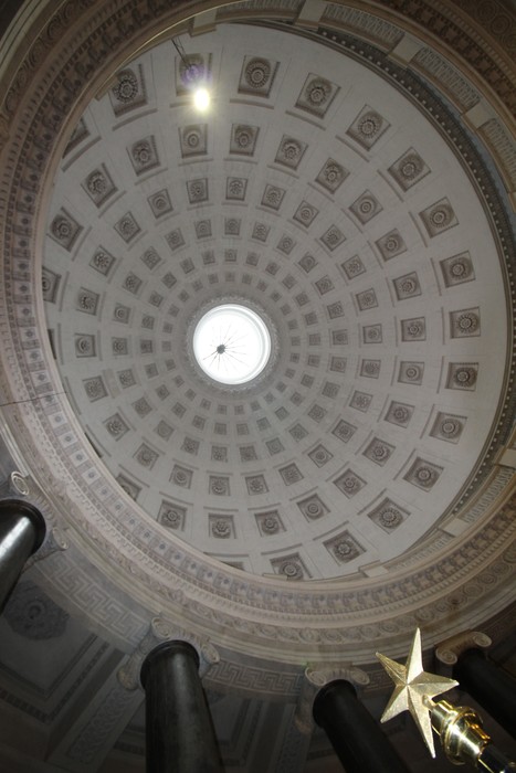 Vista dall'interno di una cupola decorata, con colonne e un'apertura centrale illuminata.