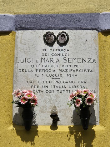 Lapide commemorativa dedicata ai coniugi Semenza, con fiori e immagini, in memoria delle vittime della ferocia nazifascista.