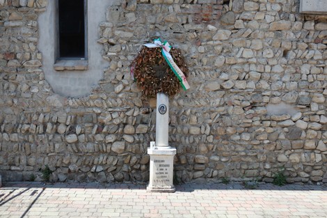 Cippo commemorativo con corona d'alloro su muro di pietra, simbolo di memoria storica e rispetto.