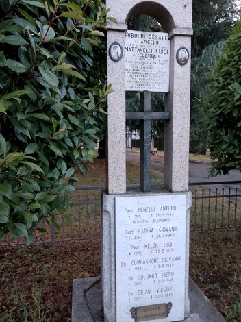 Monumento commemorativo con nomi di partigiani e deportati, circondato da vegetazione, in un ambiente sereno.