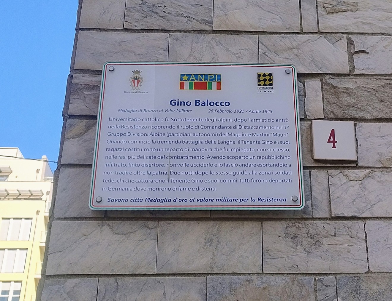 Targa in marmo con iscrizione dedicata a Gino Balocco, affissa su parete in pietra di un edificio.