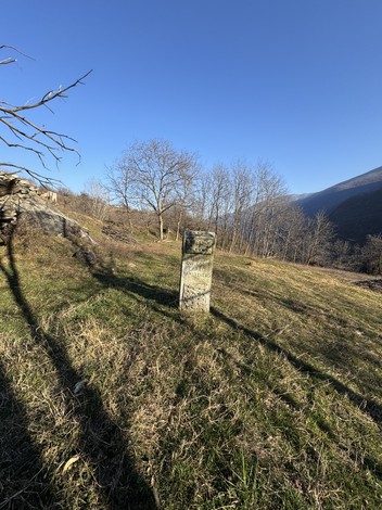 Cippo storico in un paesaggio montano, circondato da alberi spogli e un cielo sereno.