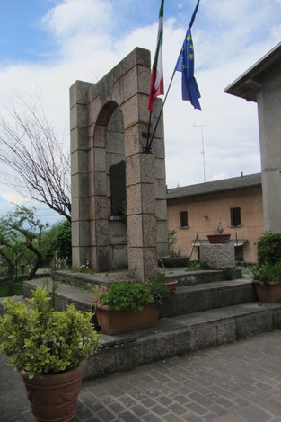 Monumento monumentale dedicato ai caduti della Resistenza, circondato da piante e bandiere.