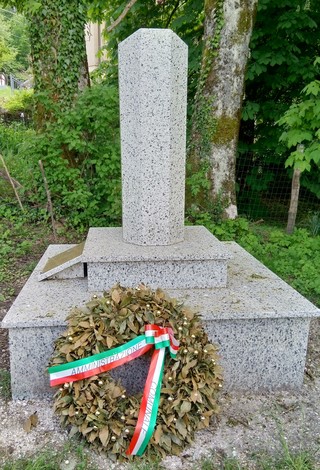 Monumento commemorativo con base in granito e corona d'alloro ai piedi, circondato da verde naturale.