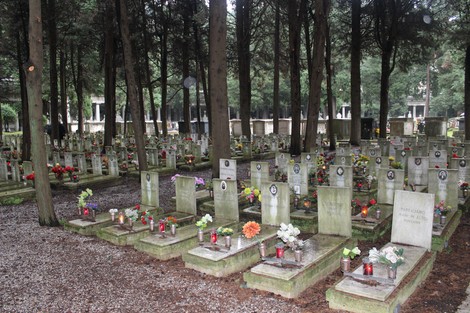 Tombe con fiori e lumini in un cimitero immerso nel verde, dedicato ai caduti per la Libertà.