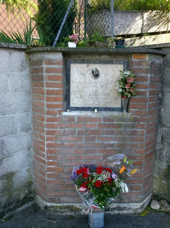 Lapide commemorativa su un muro con fiori, dedicata a Notari, in un contesto urbano.