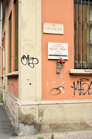 Lapide commemorativa a Prassuit, angolo di strada con fiori in omaggio e scritte sui muri.