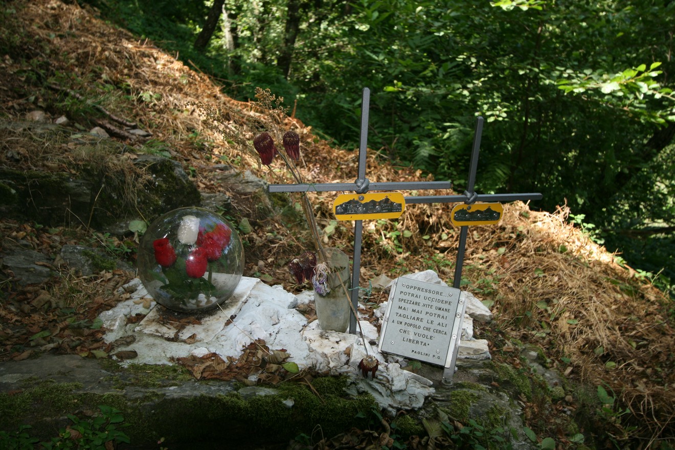 Croci commemorative in un bosco, con fiori e un messaggio di ricordo. Nature e memoria si fondono in un luogo speciale.