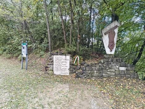 Monumento ai caduti della Pozza Rossa, circondato da una vegetazione lussureggiante e segnato da una corona d'alloro.