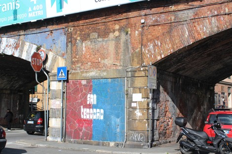 Targa su un muro sottostante un ponte, decorato con colori e scritte, in un contesto urbano.
