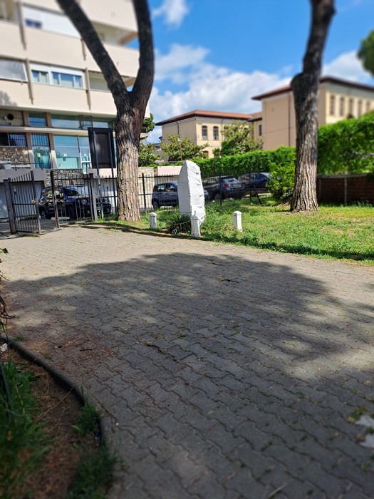 Cippo commemorativo del bombardamento di Avenza, situato in un'area verde con alberi e un vialetto in pietra.