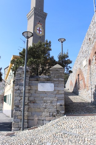Lapide commemorativa dedicata ai partigiani caduti, situata in un contesto urbano con elementi architettonici storici.
