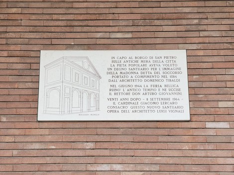Lapide bianca con bassorilievo della chiesa e lunga iscrizione, su parete di mattoni a vista.