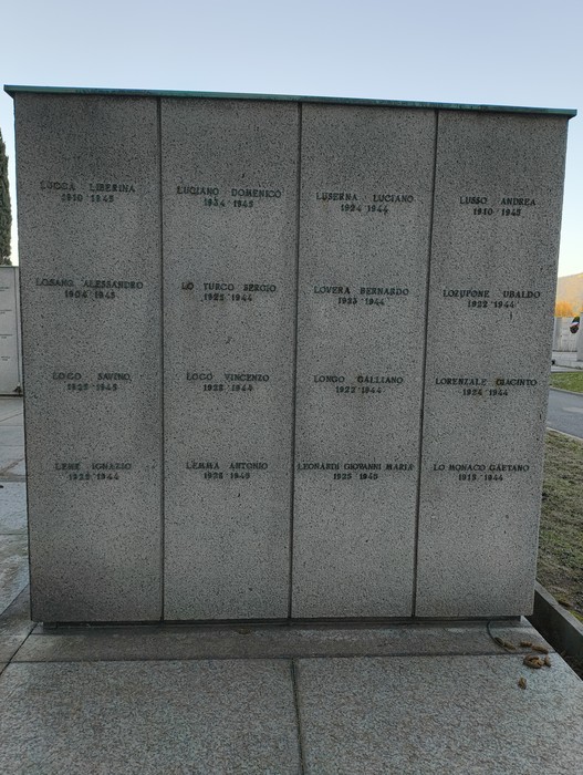 Monumento commemorativo con nomi incisi su lastre di pietra, dedicato ai caduti. Ambiente sobrio e rispettoso.