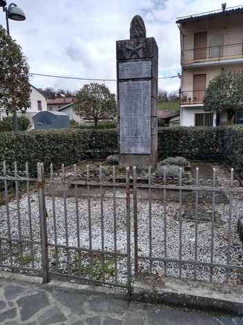 Monumento ai caduti di Roccamalatina, situato in un'area verde recintata con alberi, pietre e un cielo nuvoloso.