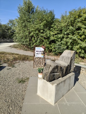 Monumento ai Martiri del Panaro, con elementi di pietra e un cartello informativo sullo sfondo verde.