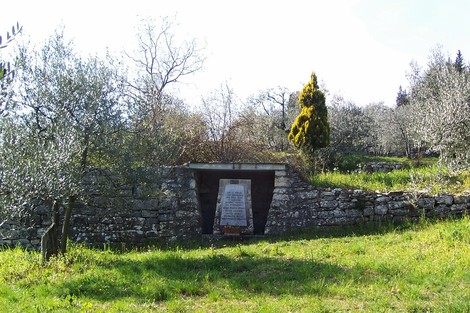 Cippo commemorativo immerso nella natura, dedicato ai caduti di Sommaia, circondato da uliveti e vegetazione.