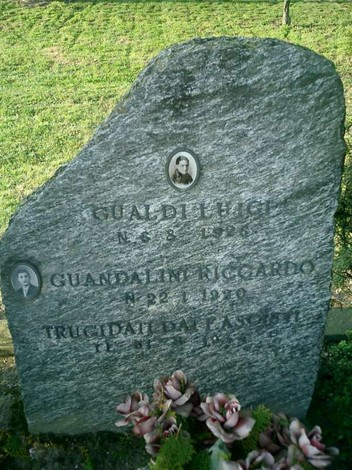 Cippo funerario in pietra con iscrizioni commemorative di Gualdi e Guandalini, circondato da vegetazione.